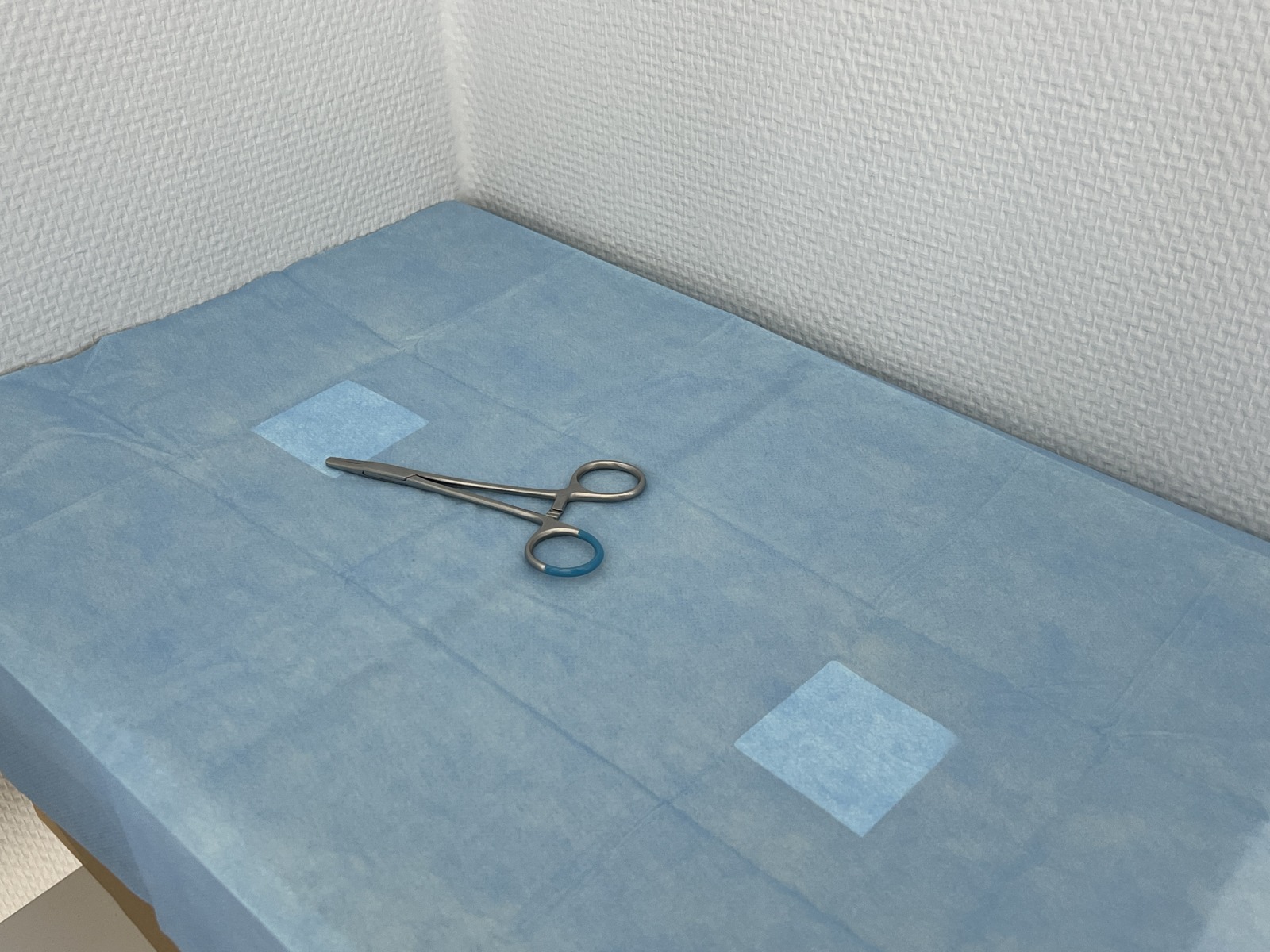Needle holder photographed from an oblique blue-background view in closed state